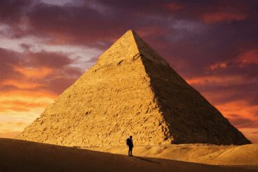 Traveler standing in front of the massive Great Pyramid of Giza at sunrise, showcasing the scale of the Ancient Wonder.