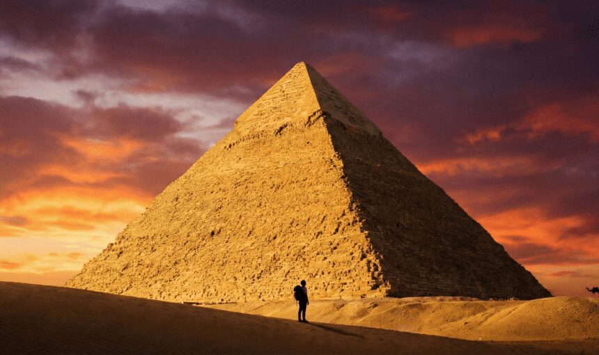 Traveler standing in front of the massive Great Pyramid of Giza at sunrise, showcasing the scale of the Ancient Wonder.