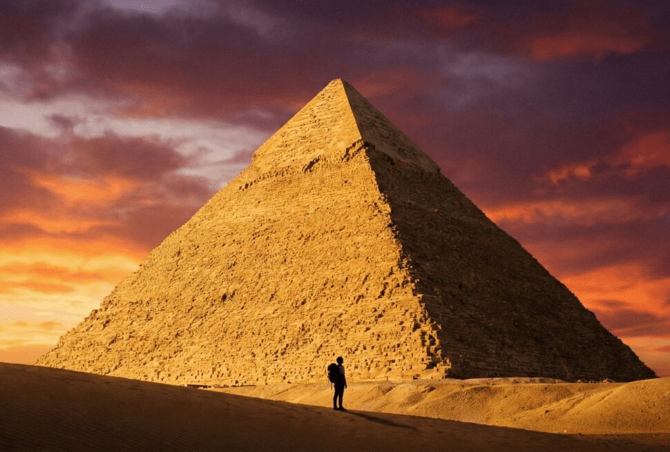 Traveler standing in front of the massive Great Pyramid of Giza at sunrise, showcasing the scale of the Ancient Wonder.